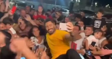 تامر حسني يخرج من سقف سيارته لالتقاط الصور مع محبيه قبل حفل الساحل.. فيديو 