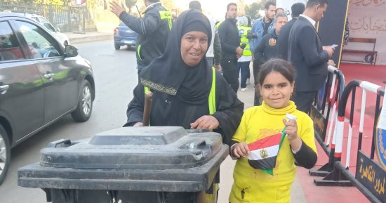 "أم شمس".. عاملة نظافة تصطحب ابنتها خلال عملها فى محيط اللجان الانتخابية
