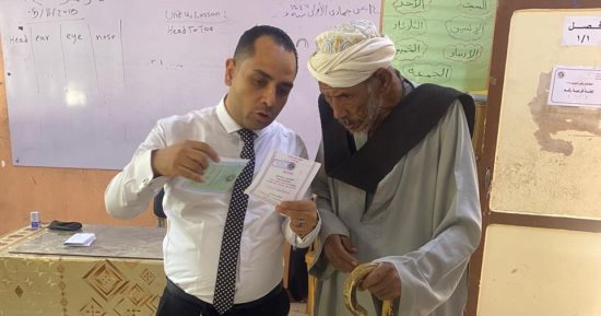 قاضٍ يساعد مسنًا فى الإدلاء بصوته داخل لجنة كيما أسوان